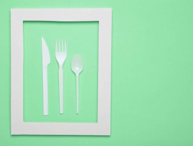 Plastik çatal bıçak takımı mavi bir arka plan üzerinde beyaz bir çerçeve içinde piknik için. Bir tek kullanımlık kaşık, çatal, bıçak. Üstten görünüm, minimalist eğilim