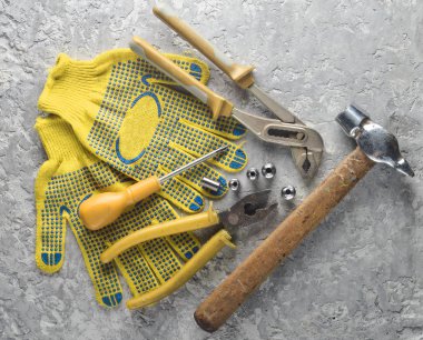 Gri bir beton yüzey üzerinde bir çalışma aracı. İş eldivenleri, çekiç, kerpeten, tornavida, pense, tornavida. Üstten görünüm