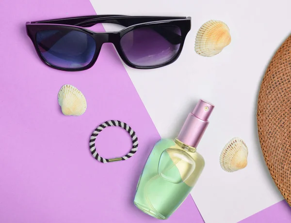 Female fashion accessories on a blue white pastel background. Sunglasses, perfume bottle, cockleshells, hat. Summer beach accessories. Top view, minimalist trend, copy space, flat lay