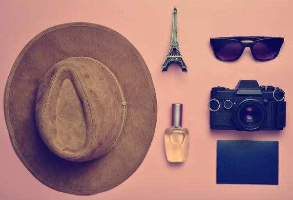 Passion for travel, wanderlust concept. Trip to France, Paris. Felt hat, film camera, sunglasses, passport, perfume bottle, souvenir statuette of the Eiffel Tower layout on a pink  paper background