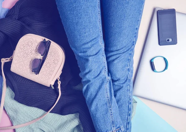 A girl in jeans sits on the floor among gadgets and accessories. Top view.