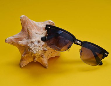 Bir büyük muslin kabuk ve sarı bir arka plan üzerinde güneş gözlüğü. Sahilde rahatlatıcı kavramı.