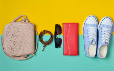 Kadın ayakkabı ve moda aksesuarları mavi sarı pastel arka plan üzerinde. Spor ayakkabı, bir çanta, çanta, kemer, güneş gözlüğü. İlkbahar Yaz koleksiyonu. Minimalizm eğilimini. Seyahat kavramı.
