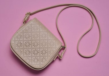 Pastel pembe bir arka plan üzerinde uzun bir kayış üzerinde bej deri çanta. Bayan aksesuarlar. Üstten görünüm.