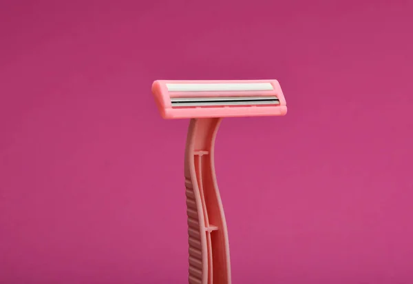 Pink disposable razor for depilation on a pink background.