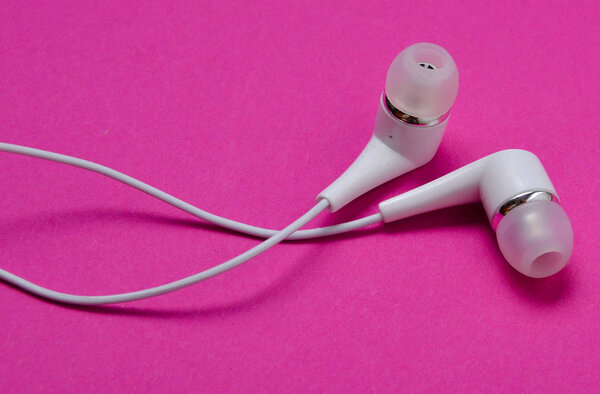 White vacuum headphones close-up on a pink background.