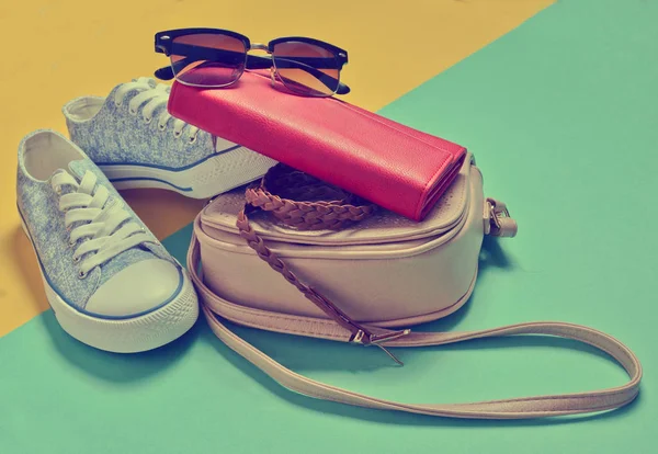 Keds, güneş gözlüğü, kemer, çanta, çanta üzerinde bir mavi sarı pastel arka plan. Bayan aksesuarlar. Minimalizm eğilimini.