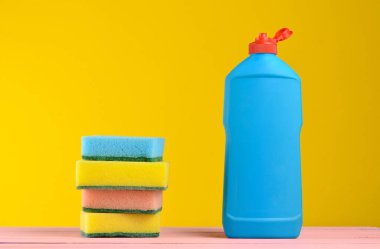 Bir şişe bulaşık yıkama, süngerler, çerçevede bir sarı duvar, tahta pastel renk masada spac kopyalayın.