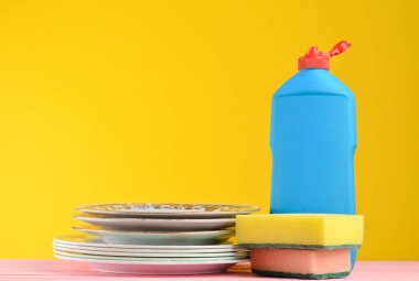 Bir şişe bulaşık yıkama, süngerler, mutfak eşyaları çerçevede bir sarı duvar, tahta pastel renk masada spac kopyalayın.