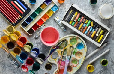 Resimlerinde bir gri beton zemin üzerinde çizim için sanatsal araçları. Palet, guaş, yağlı boya, fırça, renkli boya kalemi, pastel, renkli kalemler. Üstten görünüm