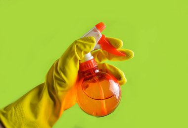 Sarı lastik eldiven elinde yeşil bir arka plan üzerinde kırmızı sprey şişe tutan