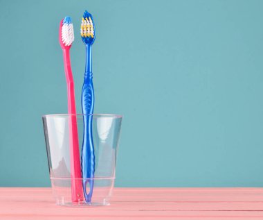 Pastel mavi arka plan üzerinde kopya alanı, minimalis banyoda şeffaf plastik bir kap içinde iki diş fırçaları