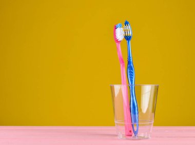 Sarı arka plan üzerinde kopya alanı, minimalis banyoda şeffaf plastik bir kap içinde iki diş fırçaları