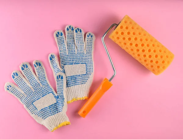 Paint roller and work gloves on a pink background. The concept of work at home, top vie