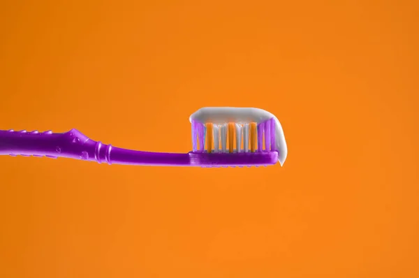 Zahnpasta Auf Einer Violetten Zahnbürste Nahaufnahme Auf Orangefarbenem Hintergrund — Stockfoto