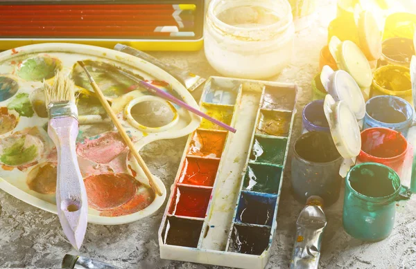 Artistic tools for drawing paintings on a gray concrete background. Palette, gouache, oil paint, brushes, colored crayons, pastel, colored pencils.