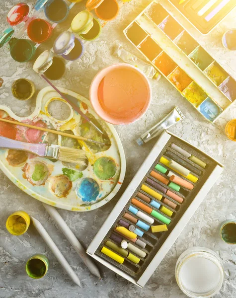 Artistic tools for drawing paintings on a gray concrete background. Palette, gouache, oil paint, brushes, colored crayons, pastel, colored pencils. Top view