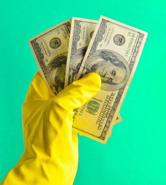 Temizlik için sarı lastik eldiven ile erkekler el yüz dolarlık banknot mavi bir arka plan üzerinde tutun. Wor için ödeme