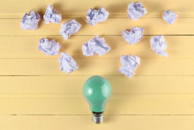 Renkli bir akkor ampul ve buruşuk beyaz kağıt topları pembe ahşap bir masa üzerinde. İdeolojik kavramı, top vie