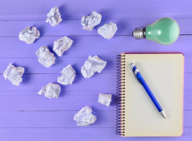 Bir kalem, akkor ampul ve pembe ahşap bir masa üzerinde buruşuk beyaz kağıt topları ile not etmek. İdeolojik kavramı, top vie