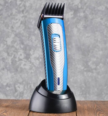 Bir meme ile kablosuz bir kırpma makası gri beton duvar adam ahşap bir masaya bir şarj istasyonu üzerinde duruyor