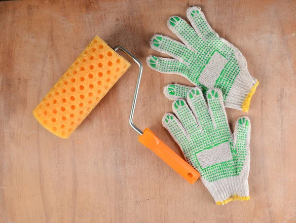 Paint roller and work gloves on a wooden background. The concept of work at home, top vie