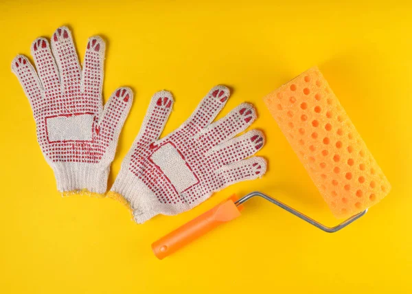 Paint roller and work gloves on a yellow background. The concept of work at home, top vie
