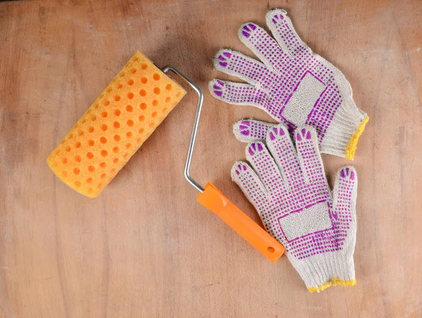 Paint roller and work gloves on a wooden background. The concept of work at home, top vie