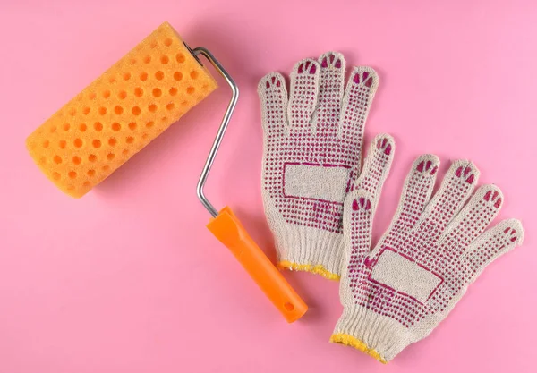 Paint roller and work gloves on a pink background. The concept of work at home, top vie