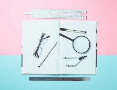 Notlar ve çizim için bir büyük defter ile ileti örneği nesneleri pastel bir arka plan üzerinde bir öğrenci için. Cetvel, marker, kalem, Büyüteç Camı, pergel, gözlük. Üstten görünüm.