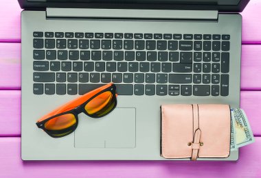 Web iş yerinde bir plaj tesisi kavramı freelancing. Dizüstü bilgisayar, güneş gözlüğü, çanta mor renk ahşap bir masa üzerinde. Üstten görünüm.