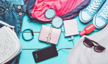 Kadın moda aksesuarları, Ayakkabı, giyim ve mavi ahşap arka plan üzerinde modern araçlar. Kot pantolon, çanta, Ayakkabı, smartphone, akıllı bilezik, güç banka, kozmetik, güneş gözlüğü, eşarp. Üstten Görünüm.