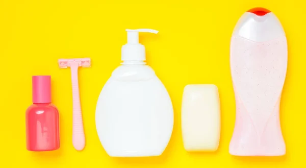 Products for the care of body, hair and personal hygiene on a yellow background. A bottle of fragrant perfume, lotion, shampoo, soap, razor. Top view. Trend of minimalism. Flat lay.