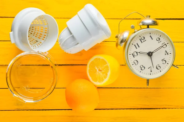 Morning fresh juice from lemon and orange. Handmade juicer, alarm clock, citrus fruit on a yellow wooden background. Top view.