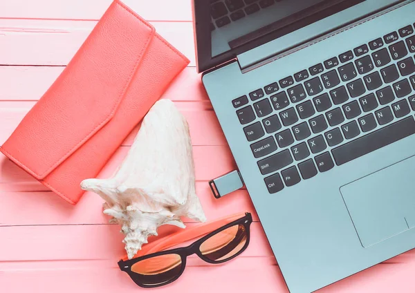 The concept of web work at a beach resort, freelancing. Laptop, flash drive, sunglasses, shell, purse on a pink color wooden table. Top view.
