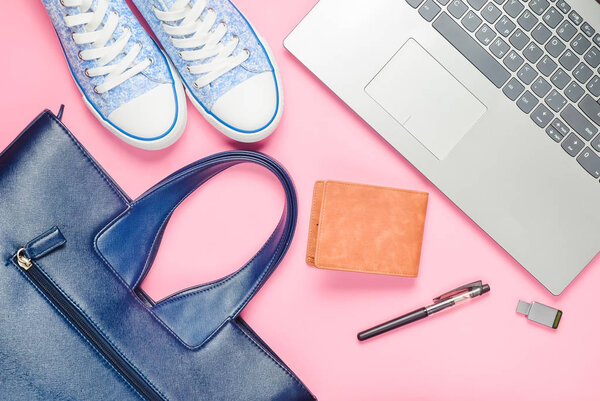 Laptop, usb flash drive and fashionable female accessories on a pink background: bag, wallet, sneakers, bag. Top view. Flat lay.