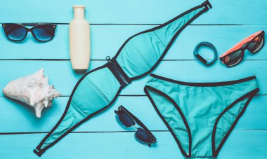 Beach resort ve mavi ahşap arka plan üzerinde Araçlar için aksesuarlar. Mayo, akıllı bilezik, Güneş kremi, güneş gözlüğü, kabuk. Üstten görünüm.