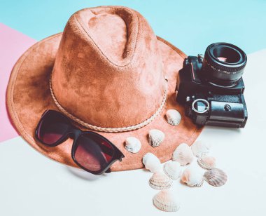 Sahilde bir tatil kavramı. Keçe şapka, güneş gözlüğü, vintage film kamerası, deniz kabuklarını renkli kağıt arka plan üzerinde.