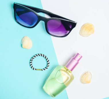 Kadın moda aksesuarları pastel mavi beyaz arka plan üzerinde. Güneş gözlüğü, parfüm şişesi, kabukları. Yaz plaj aksesuarları. Üstten görünüm, minimalist trend, kopya alanı, düz yatıyordu.