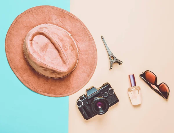 Passion for travel, wanderlust concept. Trip to France, Paris. Felt hat, film camera, sunglasses, perfume bottle, souvenir statue of Eiffel Tower layout on a colored paper background. Flat lay.