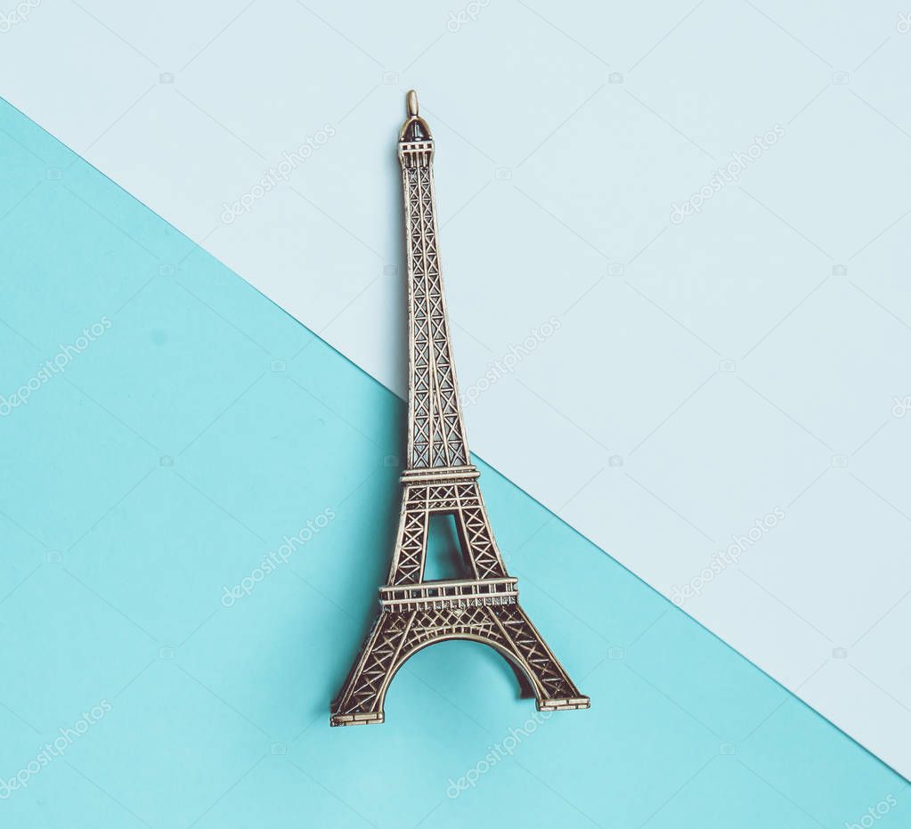 A souvenir statuette of the Eiffel Tower on a white blue pastel background. Top view. Minimalist trend.