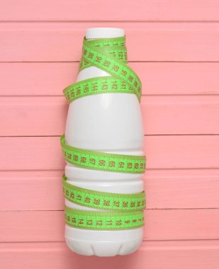 Bir cetvel üzerinde pembe bir ahşap masa, diyet, zayıflama kavramı yoğurt şişe sarılı, top vie