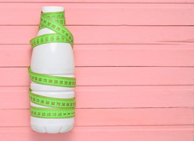 Bir cetvel üzerinde pembe bir ahşap masa, diyet, zayıflama kavramı yoğurt şişe sarılı, top vie