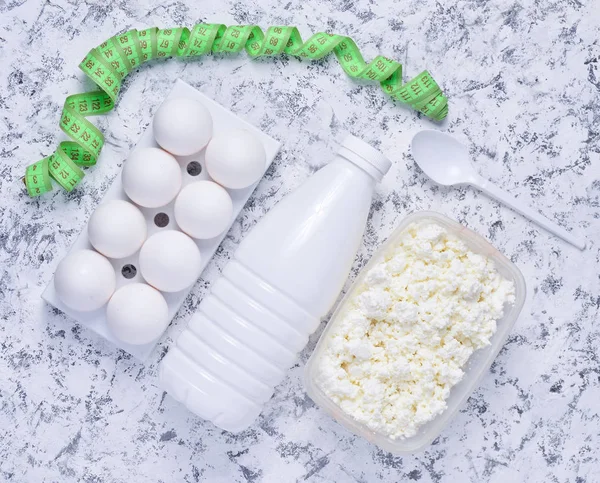 Diet, healthy food. Bottle of yogurt, cottage cheese, plastic egg tray on a white concrete background. Ruler for waist measurement. The concept of losing weight, top view, flat la