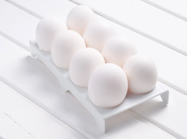 Plastic tray with white eggs on a white  wooden table, minimalism tren