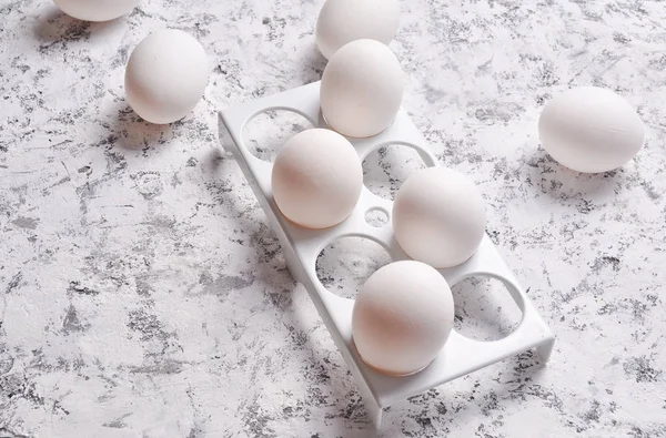 Plastic tray with white eggs on a white concrete backgroun