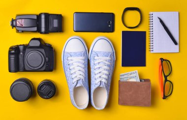 Becerikli ve aksesuarları düzen sarı bir arka plan üzerinde. Spor ayakkabı, fotoğrafik donanımlar, çanta ile dolar, akıllı saat, smartphone, defter, güneş gözlüğü. Seyahat, nesneleri, üst kavramı vie