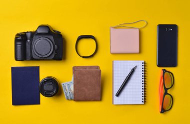 Becerikli ve aksesuarları düzen sarı bir arka plan üzerinde. Enerji banka, fotoğrafik donanımlar, çanta ile dolar, akıllı saat, smartphone, defter, güneş gözlüğü. Seyahat, nesneleri, üst kavramı vie