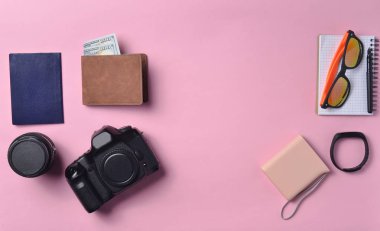 Becerikli ve aksesuarları pastel pembe düzen. Fotoğrafik donanımlar, dolar, akıllı saat, smartphone, defter, güneş gözlüğü, pasaport, güç banka ile çanta. Kavram seyahat, kopya girintili