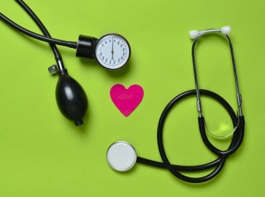 Kardiyoloji kavramı. Tıbbi monometer, stetoskop, dekoratif kalp yeşil bir arka plan üzerinde. Üstten görünüm